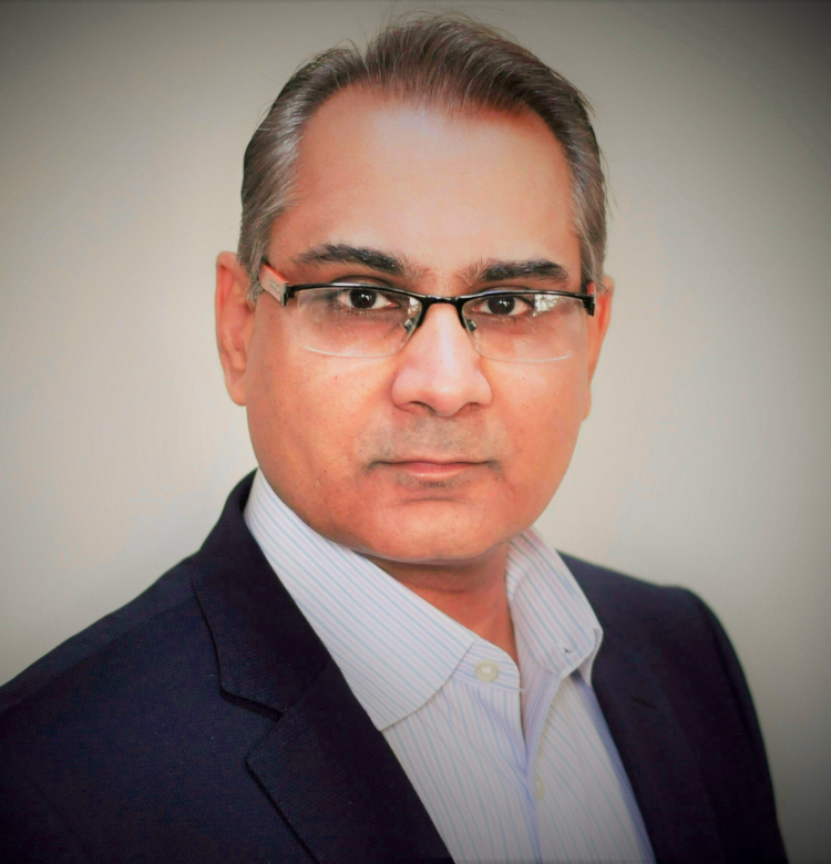 Professional head-and-shoulders portrait of a man in a suit and glasses looking at the camera, neutral background